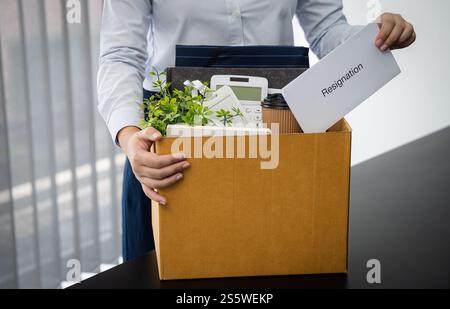 Geschäftsfrau, die Kündigungsschreiben und Verpackungsmaterial schickt, kündigen Depression oder trägt Geschäftskarton am Schreibtisch im Büro. Wechsel des Jobs oder Stockfoto