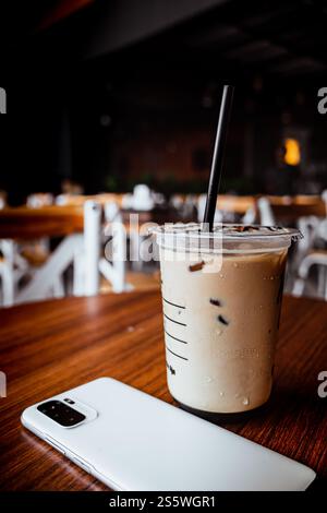 Eiskaffee Latte serviert in einem Plastikbecher neben einem Mobiltelefon auf einem Tisch in einem Café. Urbaner Lebensstil. Stockfoto