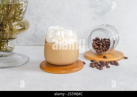 Kalter Espresso mit kalter Milchschaum, braunem gemahlenem Kaffee und Kaffeebohnen auf einem weißen Tisch Stockfoto