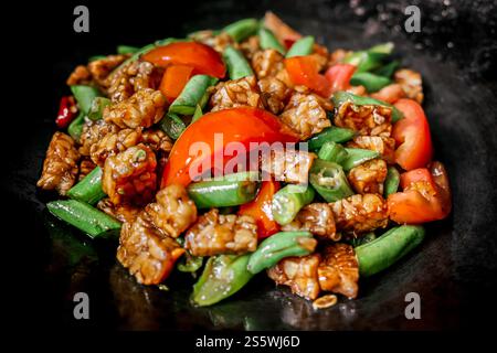 Nahaufnahme der köstlichen indonesischen Speisekarte mit Tempeh und Bohnen mit Tomatenscheiben, die auf einer Pfanne gebraten werden Stockfoto