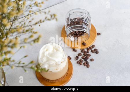 Kalter Espresso mit kalter Milchschaum, braunem gemahlenem Kaffee und Kaffeebohnen auf einem weißen Tisch Stockfoto
