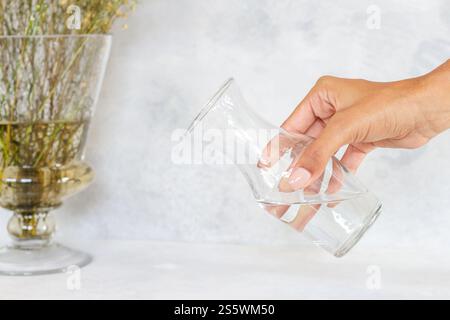 Mädchen hält Glasbecher mit Wasser zum Servieren auf dem Tisch, weißer Hintergrund isoliert mit Textur Stockfoto