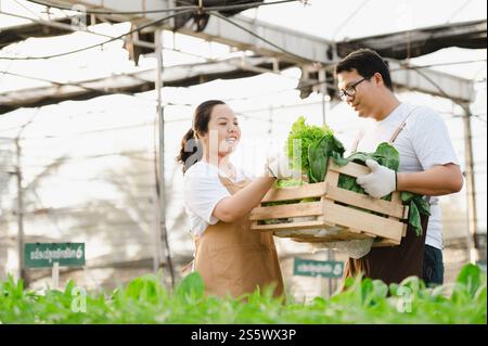Porträt eines asiatischen Bauern-Mannes und einer Frau, die eine Holzkiste voller frisches rohes Gemüse halten. Bio-Bauernkonzept. Stockfoto