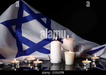 Brennende Kerzen mit Stacheldraht und großer Flagge Israels auf dunklem Hintergrund. Holocaust-Gedenktag Stockfoto