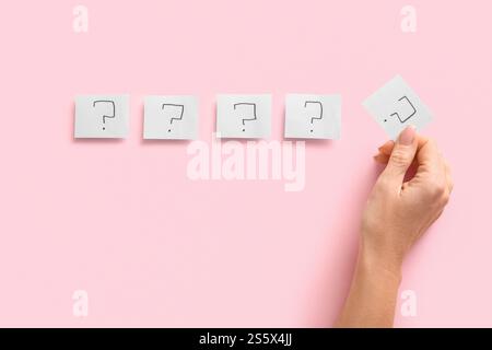 Weibliche Hand- und Papierbögen mit Fragezeichen auf rosa Hintergrund, Nahaufnahme Stockfoto