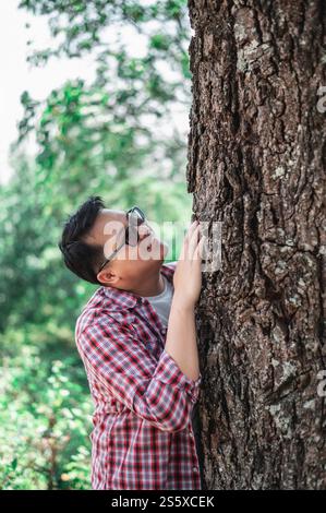 Porträt eines glücklichen asiatischen Mannes, der einen Baum im Wald umarmt. Die Natur schützen und lieben. Umwelt- und Umweltkonzept. Stockfoto