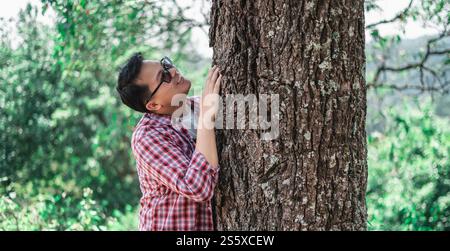 Porträt eines glücklichen asiatischen Mannes, der einen Baum im Wald umarmt. Die Natur schützen und lieben. Umwelt- und Umweltkonzept. Stockfoto