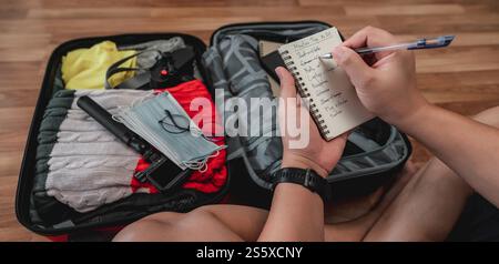 Nahaufnahme von Mann überprüft die Checkliste. Ich wählte Kleidung, Reisedokumente, die Reiseroute für eine Alleinreise. Reise-, Urlaubs- und Urlaubskonzept. Stockfoto