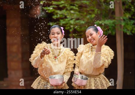 Junge lächelnde Frauen tragen wunderschöne thailändische Kostüme, spritzen Wasser in Tempel und bewahren die gute Kultur der Thailänder während Songkran Stockfoto