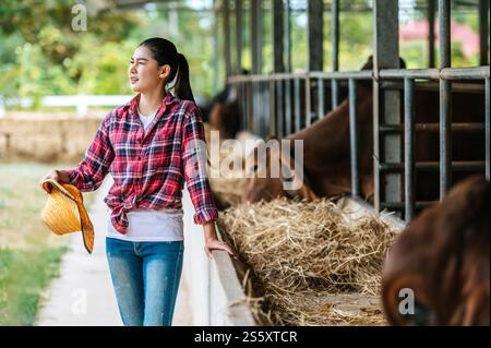 Porträt einer müden jungen asiatischen Bäuerin, die im Kuhstall auf Milchviehhof arbeitet. Landwirtschaft, Landwirtschaft, Menschen, Technologie und Tierhaltung Stockfoto