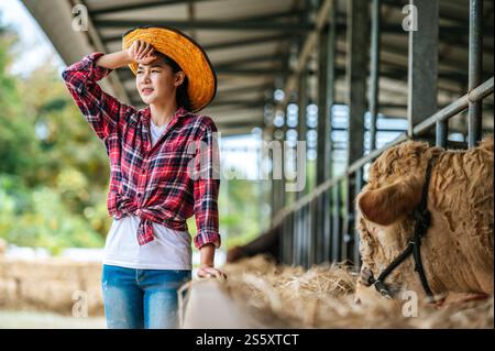 Porträt einer müden jungen asiatischen Bäuerin, die im Kuhstall auf Milchviehhof arbeitet. Landwirtschaft, Landwirtschaft, Menschen, Technologie und Tierhaltung Stockfoto