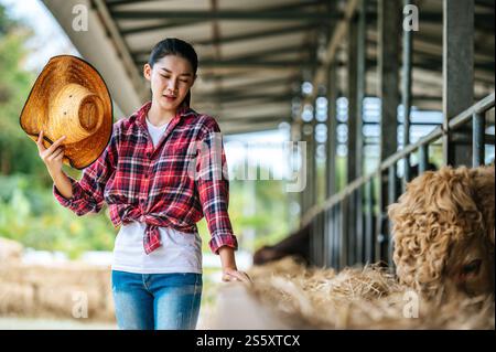Porträt einer müden jungen asiatischen Bäuerin, die im Kuhstall auf Milchviehhof arbeitet. Landwirtschaft, Landwirtschaft, Menschen, Technologie und Tierhaltung Stockfoto