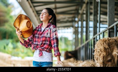 Porträt einer müden jungen asiatischen Bäuerin, die im Kuhstall auf Milchviehhof arbeitet. Landwirtschaft, Landwirtschaft, Menschen, Technologie und Tierhaltung Stockfoto
