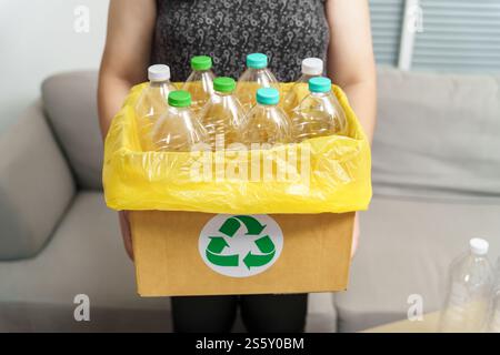 Recyceln Sie die umweltfreundliche Zero Concept Frau, die leere Plastikflasche mit gelben Mülltüten zu Hause in den Recyclingbehälter wirft Stockfoto