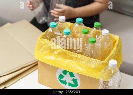 Recyceln Sie die umweltfreundliche Zero Concept Frau, die leere Plastikflasche mit gelben Mülltüten zu Hause in den Recyclingbehälter wirft Stockfoto