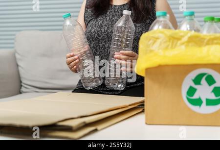 Recyceln Sie die umweltfreundliche Zero Concept Frau, die leere Plastikflasche mit gelben Mülltüten zu Hause in den Recyclingbehälter wirft Stockfoto