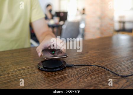 Laden des Mobiltelefonakkus mit dem drahtlosen Gerät in der Tabelle. Smartphone wird auf einem Ladepad aufgeladen. Mobiltelefon in der Nähe des kabellosen Ladegeräts Stockfoto