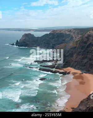 Sandstrand mit felsigen Bergrücken trübes Wetter Aussicht auf Sommer Atlantic an der felsigen Küste (Costa Vicentina, Algarve, Portugal). Und Ocean Surf Wellen. Stockfoto