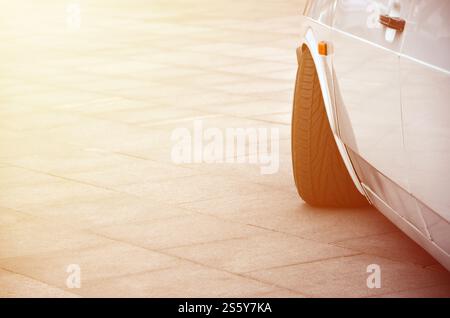 Diagonalansicht eines weißen, glänzenden Autos, das auf einem Quadrat grauer Fliesen steht Stockfoto