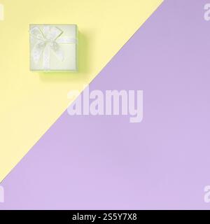 Kleine gelbe Geschenkbox liegt auf Textur Hintergrund von Mode Pastellgelb und violett Farben Papier in minimalem Konzept. Kleine gelbe Geschenkbox liegt drauf Stockfoto