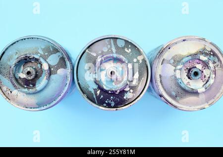 Einige gebrauchte Sprühdosen mit blauen Farbtropfen liegen auf Texturhintergrund von Mode pastellblauem Farbpapier in minimalem Konzept. Ein paar gebrauchte Sprühdosen Stockfoto