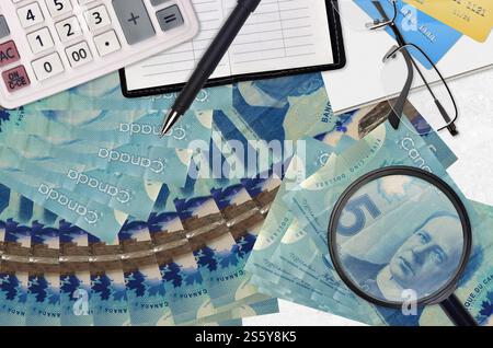 5 kanadische Dollarscheine und Taschenrechner mit Brille und Stift. Steuerzahlungssaisonkonzept oder Investitionslösungen. Job mit hohem Gehalt wird gesucht Stockfoto