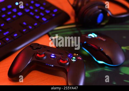 Modernes Gamepad und Gaming-Maus liegen mit Tastatur und Kopfhörern auf dem Tisch in der dunklen Spielzimmerszene aus nächster Nähe. Herausforderungen und Wettbewerbe bei Videospielen Stockfoto
