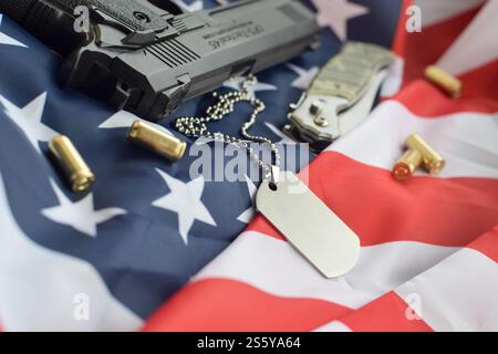 Army Dog Tag Token mit 9-mm-Kugeln und Pistole liegen auf gefalteter US-Flagge. Ein Satz von Veteranen des US-Militärs oder ein Trophäenkit für alte Zwecke. Armeehund Stockfoto
