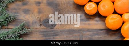 Viele Orangenmandarinen und Tannenzweige liegen auf braunen Holzdielen. Neujahrsflacher Hintergrund. Viele Orangenmandarinen und Stockfoto