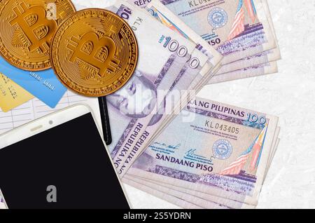 100 philippinische Piso-Scheine und goldene Bitcoins mit Smartphone und Kreditkarten. Anlagekonzept für Kryptowährungen. Krypto-Mining oder -Handel Stockfoto