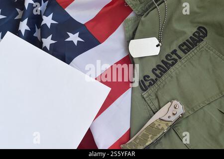 Das militärische Hundemarke und -Messer liegt auf der Uniform der alten US-Küstenwache und der gefalteten US-Flagge. Hintergrund für das Design des Coast Guard Day. Militär Stockfoto