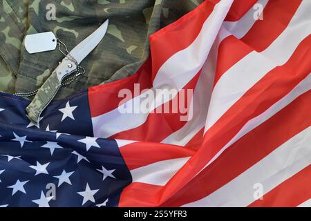 Army Dog Tag Token und Messer liegt auf Old Camouflage Uniform und gefalteter United States Flag. Hintergrund für das Design des Veterans Day. Army Dog Tag Token und Stockfoto