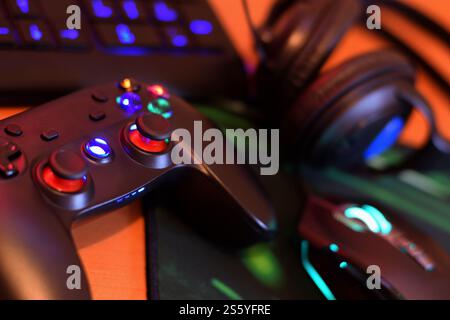 Modernes Gamepad und Gaming-Maus liegen mit Tastatur und Kopfhörern auf dem Tisch in der dunklen Spielzimmerszene aus nächster Nähe. Videospielsucht bei Jugendlichen Stockfoto