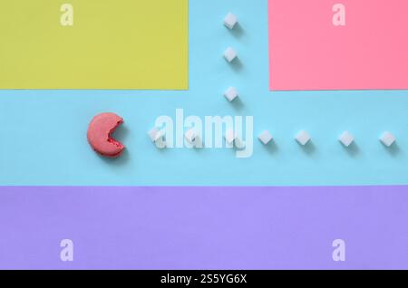 Eine Komposition aus Makronen mit offenem Mund, die Zuckerwürfel auf blauem, rosa, gelbem und violettem Pastellhintergrund essen wird. Das Konzept von Stockfoto