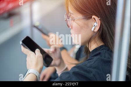 Junge asiatische Frau, die in einem U-Bahn-Auto sitzt und Musik mit ihrem Smartphone per kabellosem in-Ear hört. Selektiver Fokus. Stockfoto