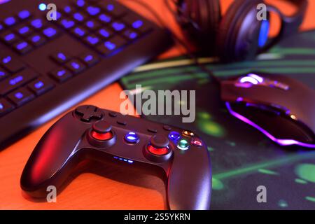 Modernes Gamepad und Gaming-Maus liegen mit Tastatur und Kopfhörern auf dem Tisch in der dunklen Spielzimmerszene aus nächster Nähe. Herausforderungen und Wettbewerbe bei Videospielen Stockfoto