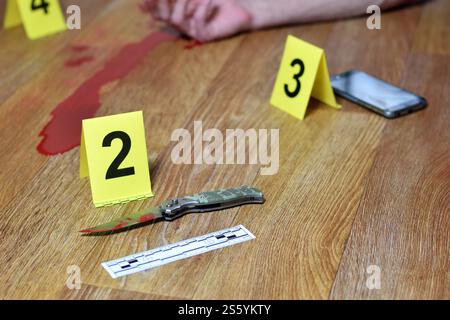 Tatortuntersuchung - blutiges Messer und Opferhand mit gelben kriminellen Markierungen auf Küchenboden. Mordbeweise. Tatortuntersuchung Stockfoto