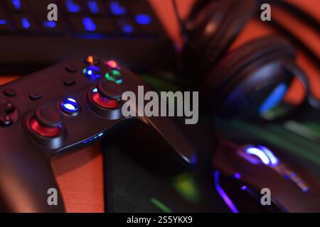 Modernes Gamepad und Gaming-Maus liegen mit Tastatur und Kopfhörern auf dem Tisch in der dunklen Spielzimmerszene aus nächster Nähe. Moderne Elektronik für Profis Stockfoto