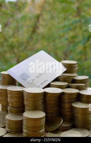 Kreditkarte auf einem großen Stapel glänzender ukrainischer alter 1 Hrywna Münzstapel aus nächster Nähe auf verschwommenem grünen Baumhintergrund. Das Konzept des Geldtransfers und Stockfoto