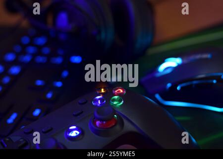Modernes Gamepad und Gaming-Maus liegen mit Tastatur und Kopfhörern auf dem Tisch in der dunklen Spielzimmerszene aus nächster Nähe. Gameplay-Streaming und Videospiele Stockfoto
