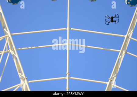 Drohne mit Fotokamera startet vom Land und fliegt für Fotos vor dem Riesenrad. Die Drohne startet vom Land und fliegt, um Fotos zu machen Stockfoto