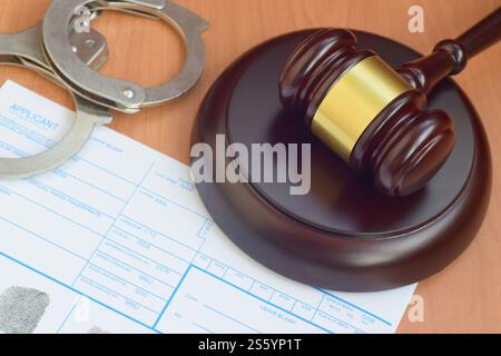 Justizhammer und Antragsteller- oder Fingerabdruckkarte mit Polizeihandschellen aus nächster Nähe. Justizhammer und Antragsteller- oder Fingerabdruckkarte bei der Polizei Stockfoto