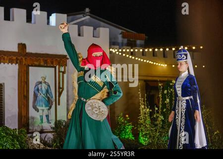 Anapa, Russland - 30. August 2024: Mann und Frau im Kaukasischen Tanz. Er in Grün mit roter Maske, mit Dolch, sie in blauem Kleid mit hohem Kopfschmuck. C Stockfoto