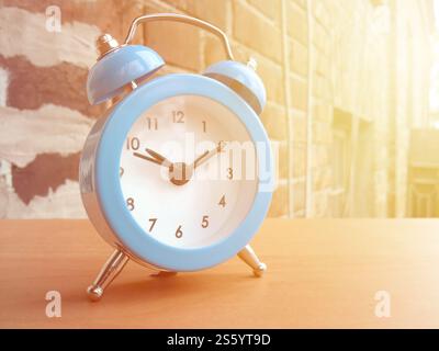 Kleiner blauer Wecker auf rotem Backsteinmauerhintergrund in der Morgensonne. Kleiner blauer Wecker auf rotem Backsteinmauerhintergrund Stockfoto