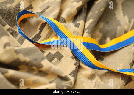 Gepixelter, digitaler Militärtarnstoff mit Band in blauen und gelben Farben. Attribute der ukrainischen patriotischen Soldatenuniform. Gepixelt digital Stockfoto