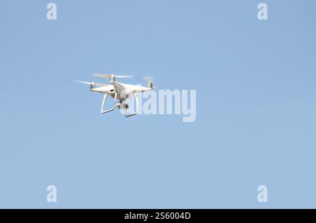 Große weiße Drohne, die in einem hellen wolkenlosen blauen Himmel schwebt, Funksteuerhubschrauber mit tragbarer Videokamera-Versorgung. Große weiße Drohne, die in A schwebt Stockfoto