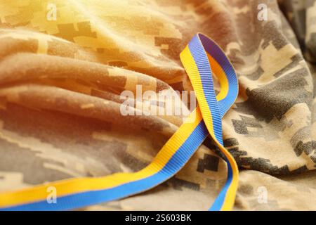 Gepixelter, digitaler Militärtarnstoff mit Band in blauen und gelben Farben. Attribute der ukrainischen patriotischen Soldatenuniform. Gepixelt digital Stockfoto
