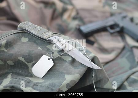 Army Dog Tag Token mit Messer und Pistole liegen auf gefaltetem grünen Stoff. Ein Set von Militärveteranen oder ein altes Trophäenkit. Army Dog Tag Stockfoto