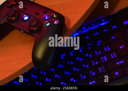 Modernes Gamepad mit pc-Tastatur auf dem Tisch in dunkler Spielzimmerszene aus nächster Nähe. Kooperatives Teamplay-Konzept. Modernes Gamepad mit eingeschalteter pc-Tastatur Stockfoto