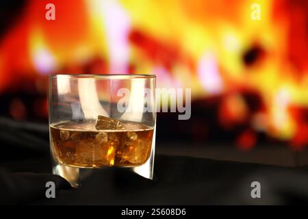 Whisky oder Whiskey oder Bourbon mit Eis auf Holzoberfläche auf Kaminhintergrund. Luxus-Elite-Alkohol im breiten Glas. Dunkle Szene mit niedriger Taste. Whisky oder Stockfoto
